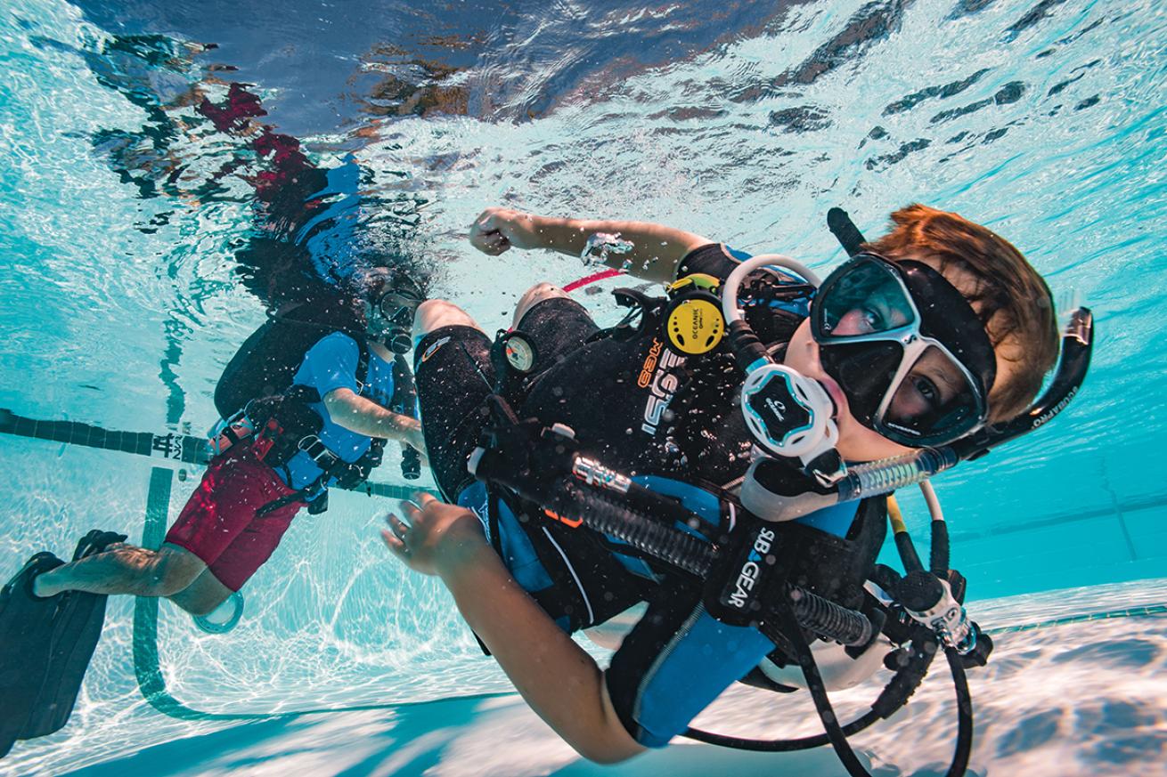 Young male diver swims underwater in a pool during a training sesson.