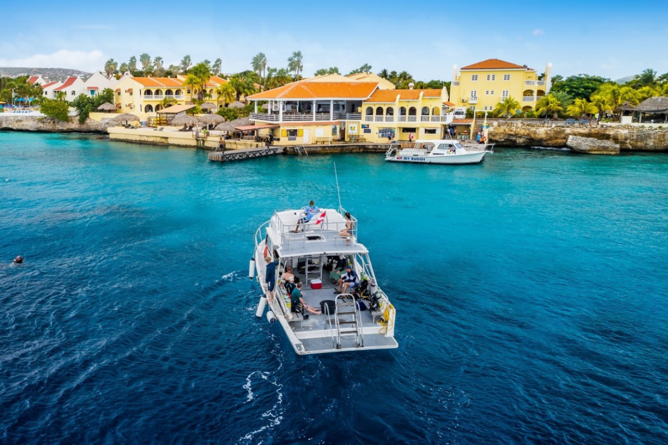 A dive boat approaching a dock at resort with yellow buildings