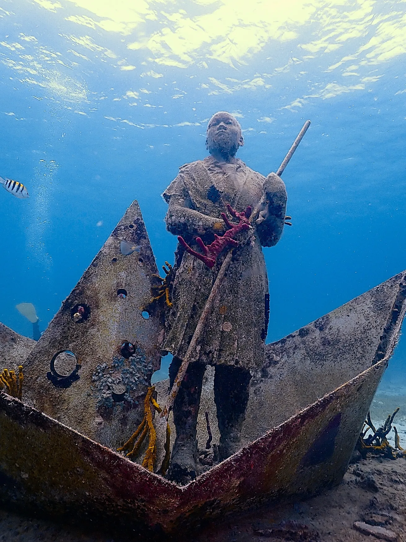 a sculpture of a child standing in a large paper boat with holes in the sails and holding a paddle