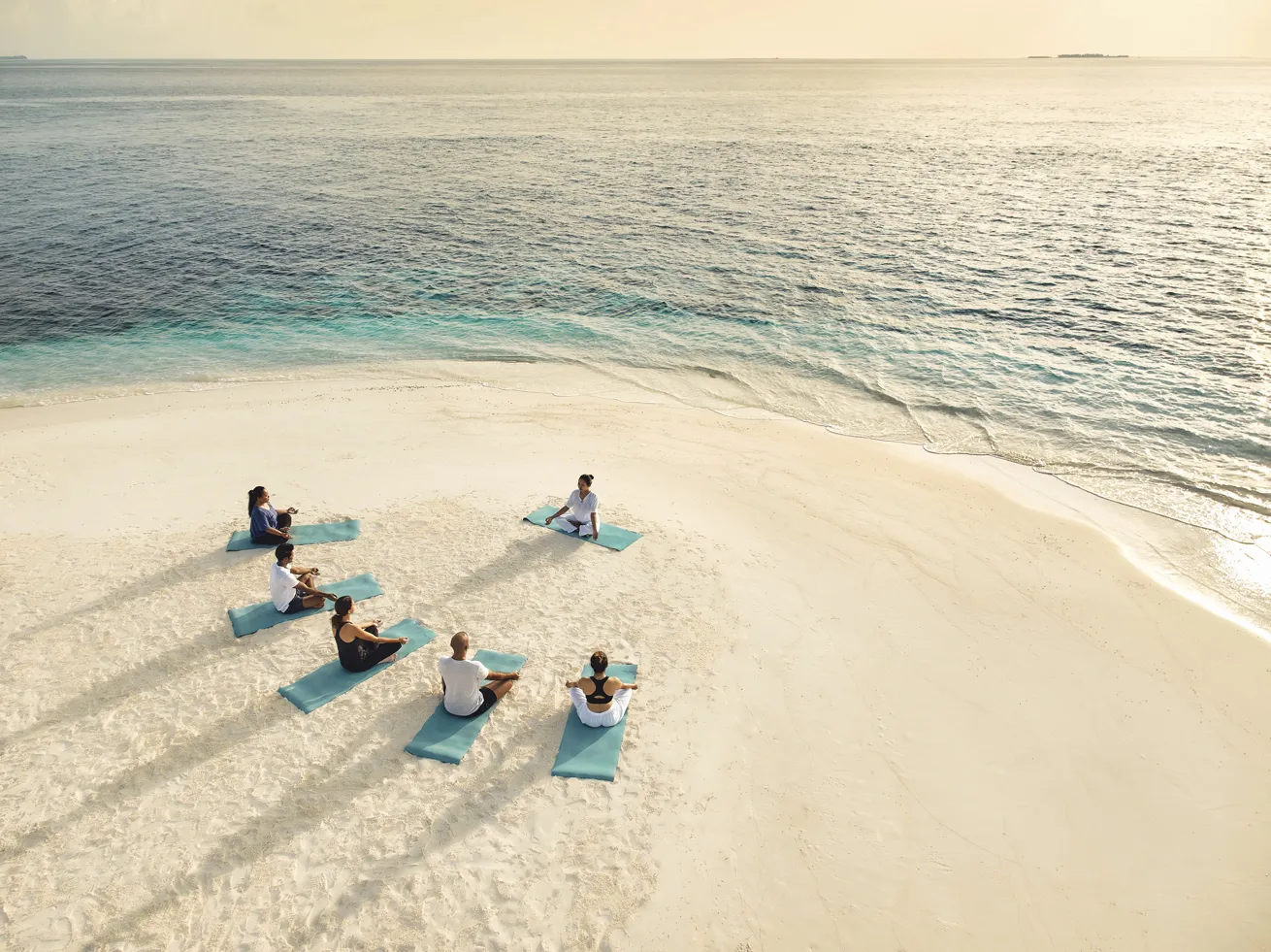 a group of people practicing yoga on the beach in maldives