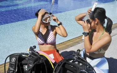 women-by-pool-putting-on-masks.jpg.webp