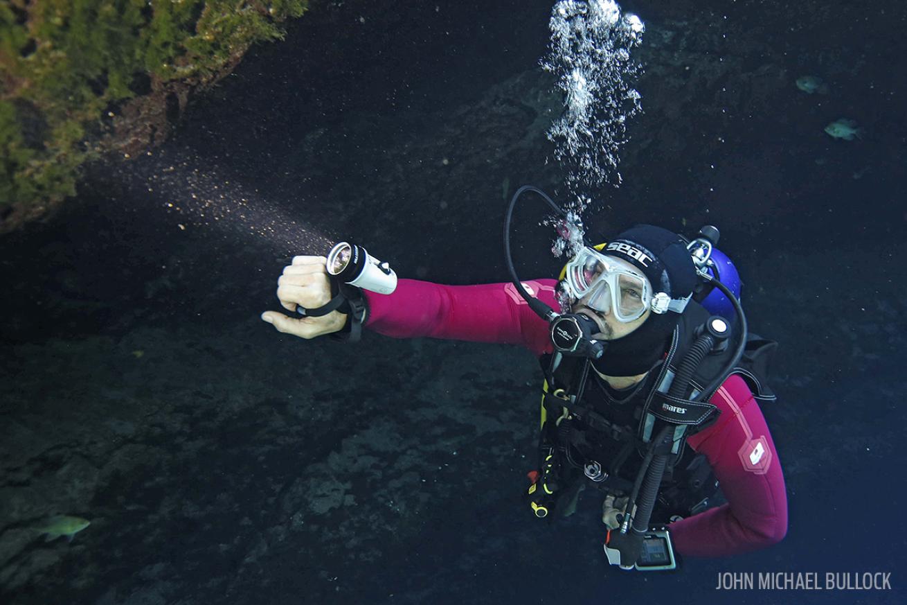 ScubaLab Director shines dive light underwater in cave