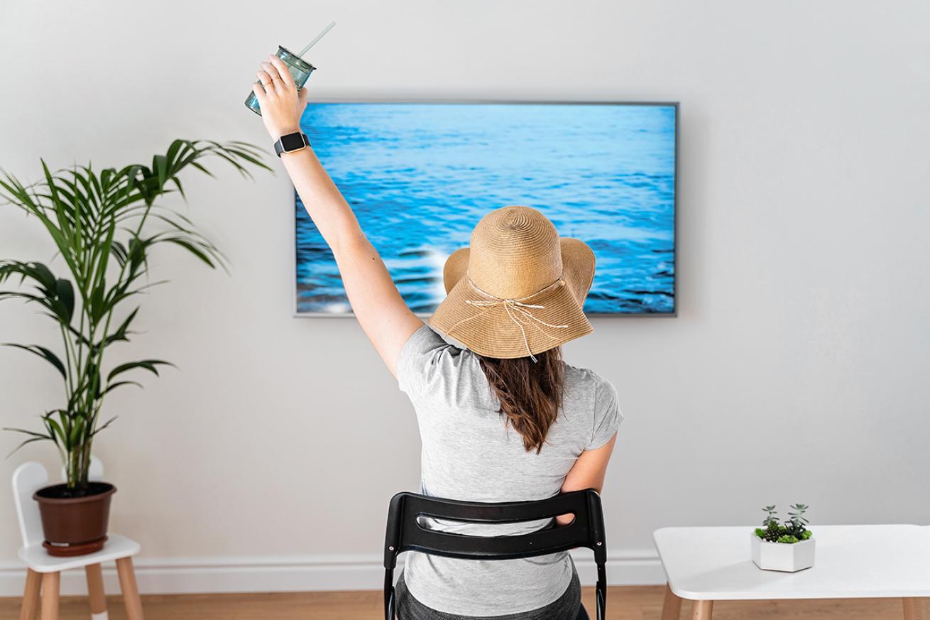 Woman pretends to be on beach by watching ocean on TV.