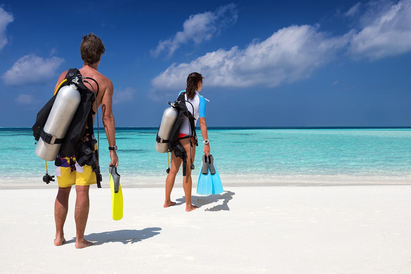 Divers stand apart on the beach looking at the water