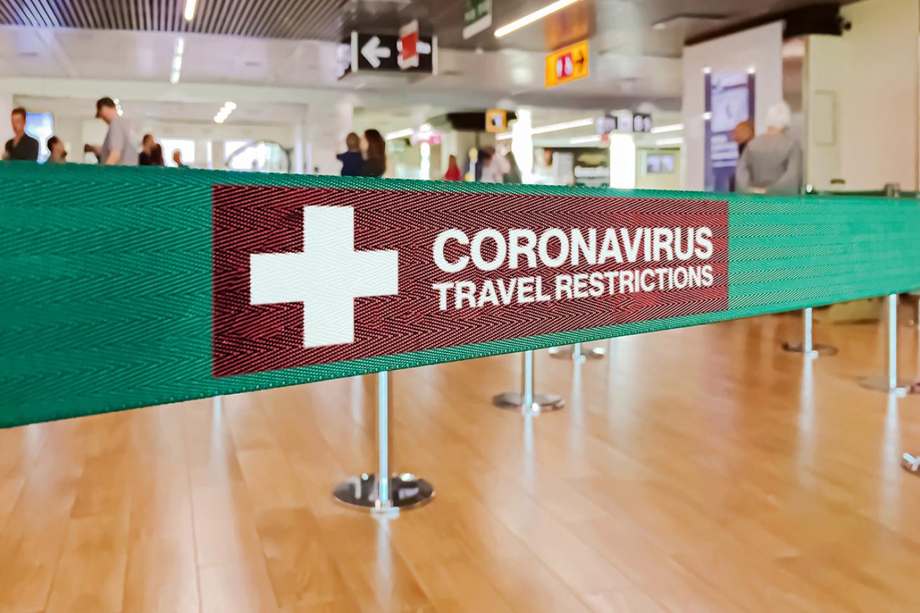 Green ribbon barrier inside an airport with the warning of travel restrictions due to coronavirus.