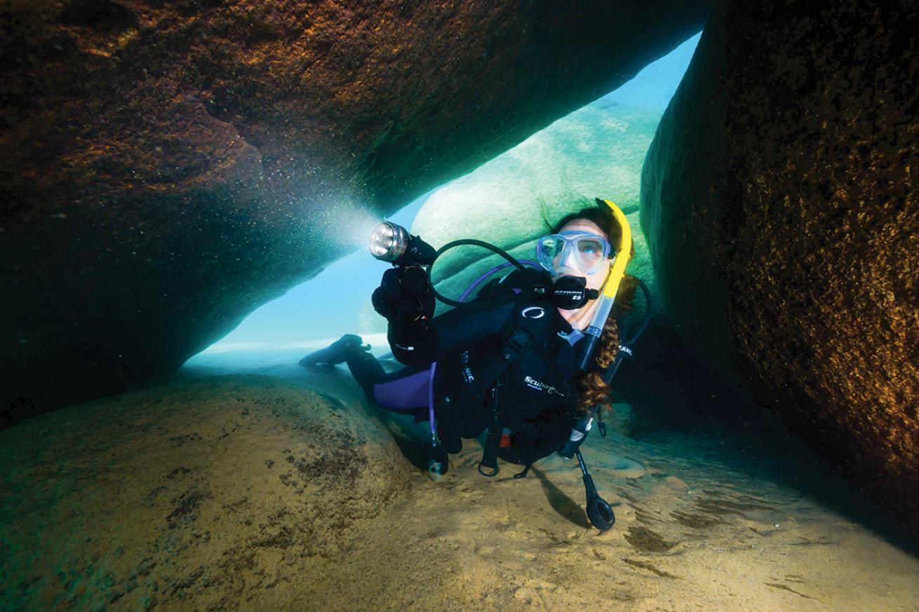 A diver shines her light to light up a submerged rock enclosure in Lake Tahoe.