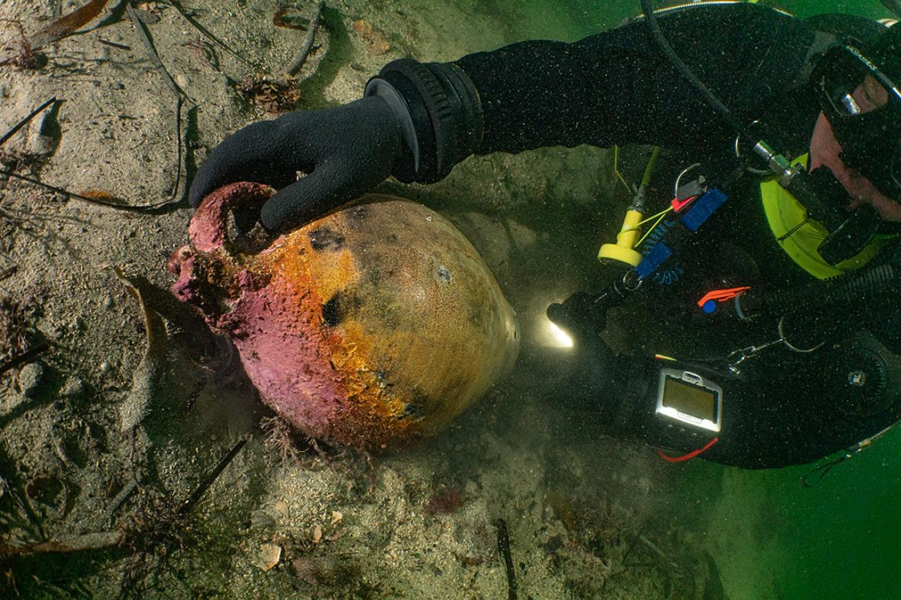 A diver shines a flashlight on a jug from the shipwreck.