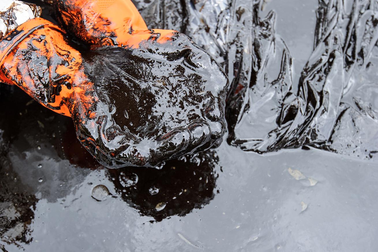 Gloved hands pick up crude oil from a spill.