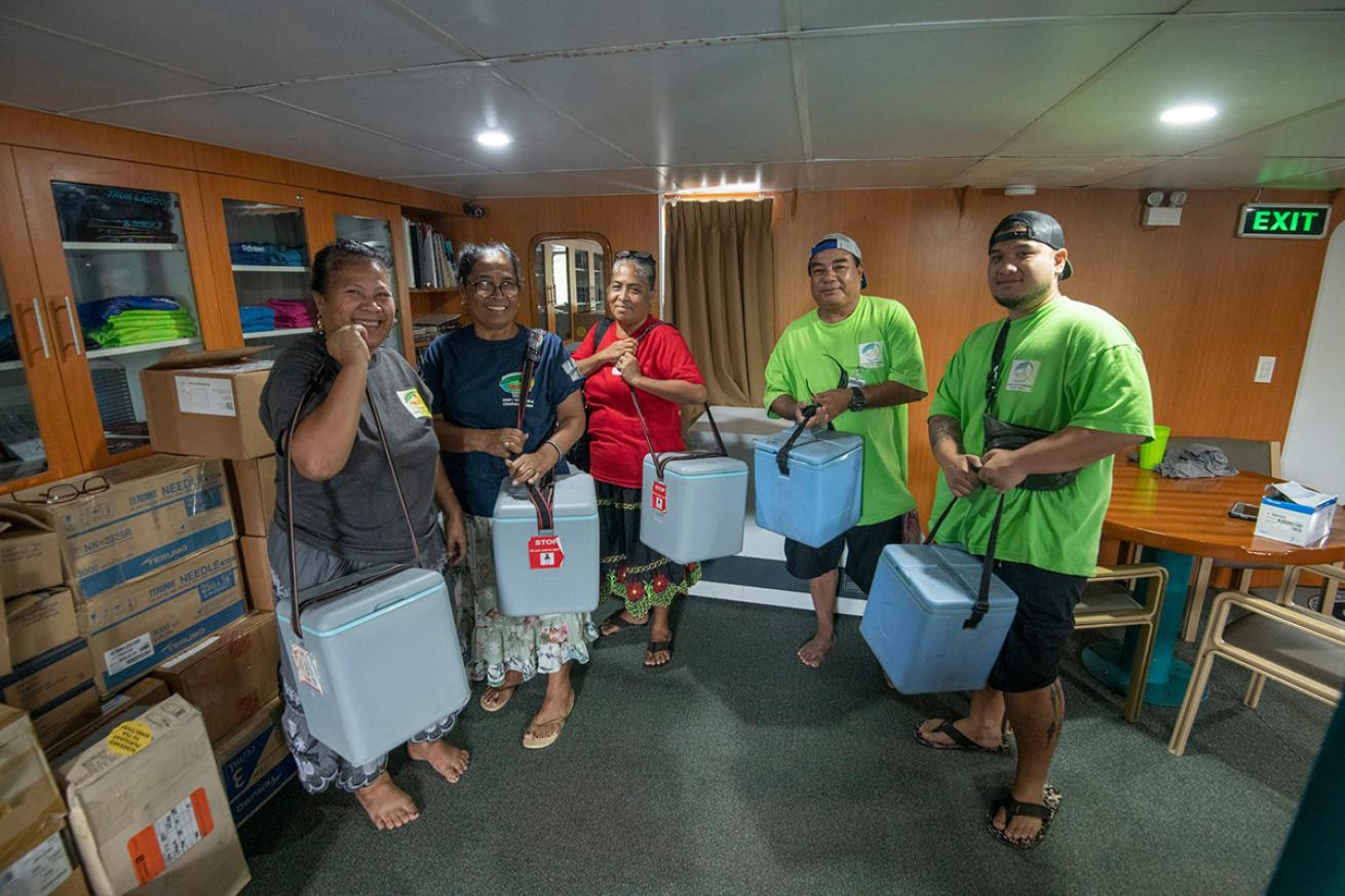 Micronesian health workers hold coolers while standing in the salon of a liveaboard.