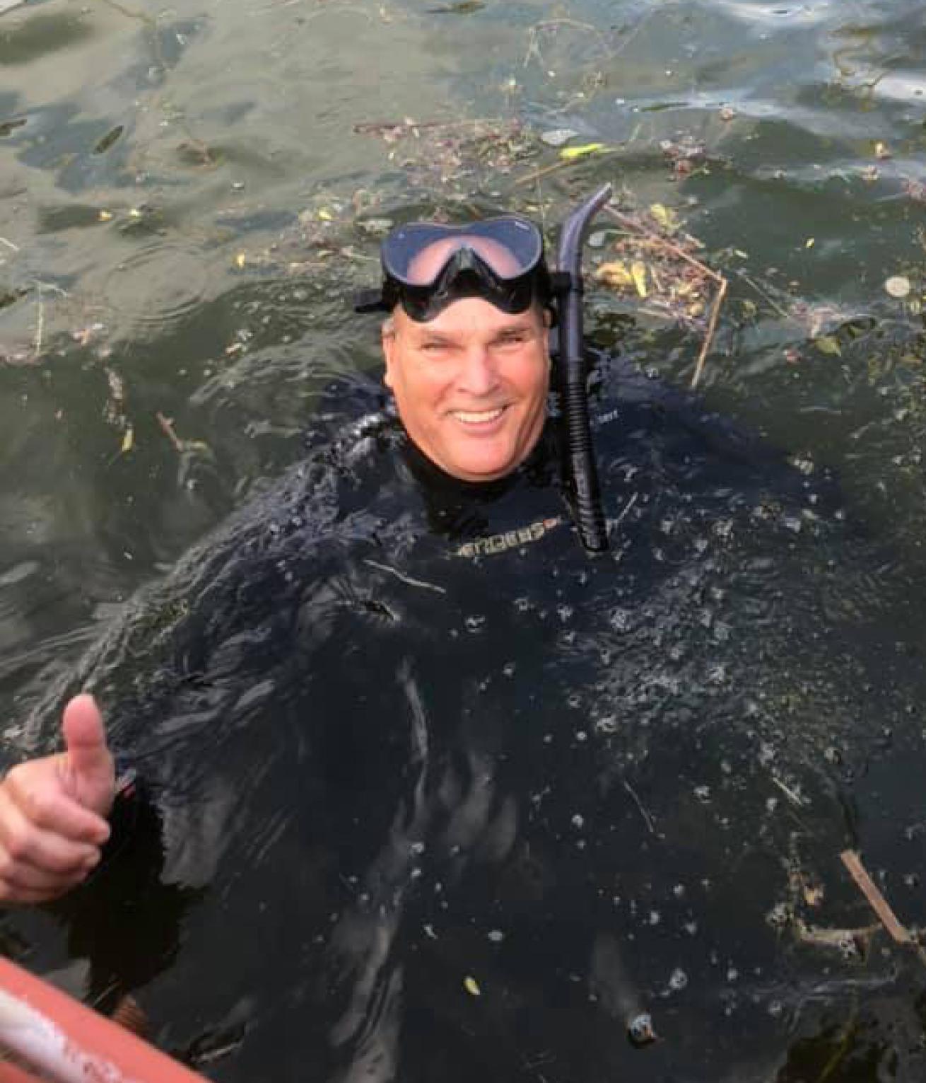Robert Grattan gives a thumbs up from the water while wearing a wetsuit