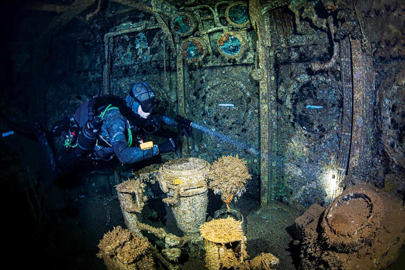 A diver shines a flashlight inside the Saratoga wreck.