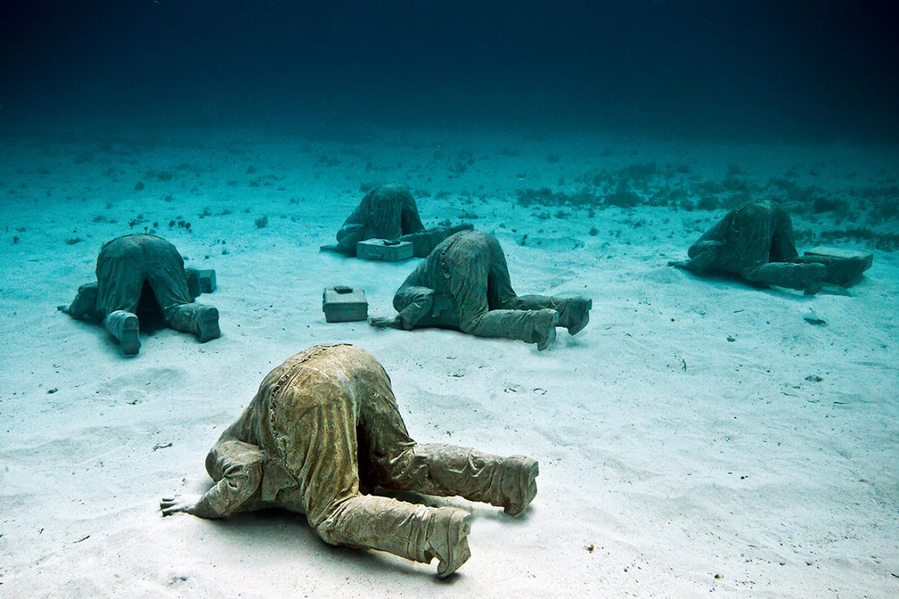 Statues of men in suits burring their heads in the seafloor