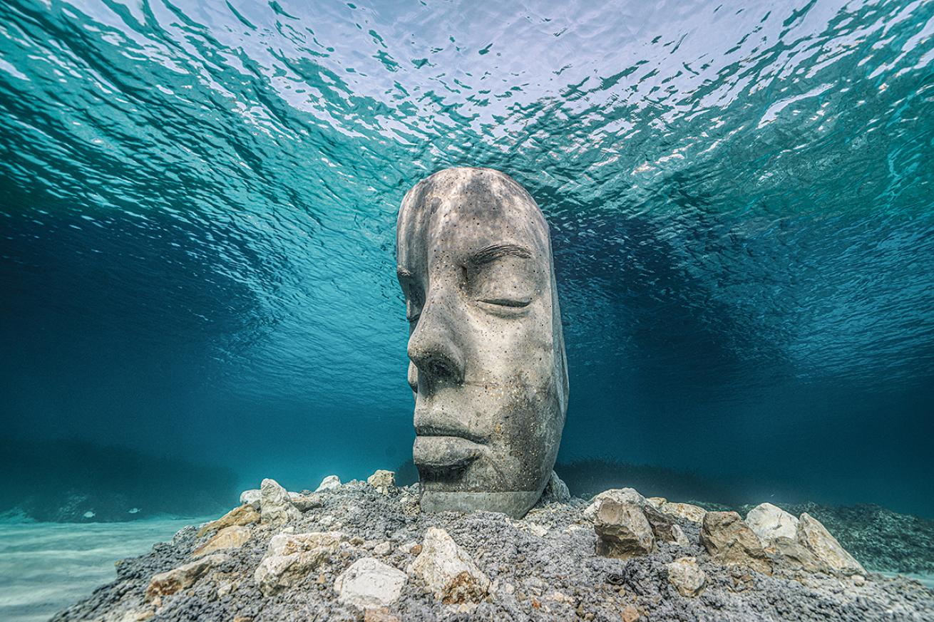 A six-foot statue of a face split down the middle sits on the seafloor