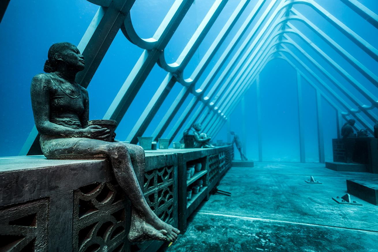 The statue of a woman sits on a concrete block in a concrete conservatory structure underwater