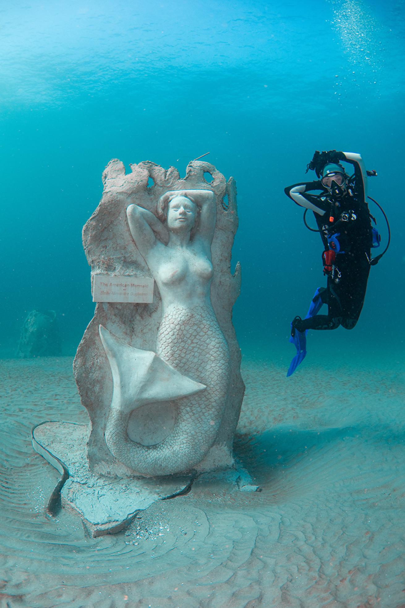 A diver poses next to an underwater mermaid statue