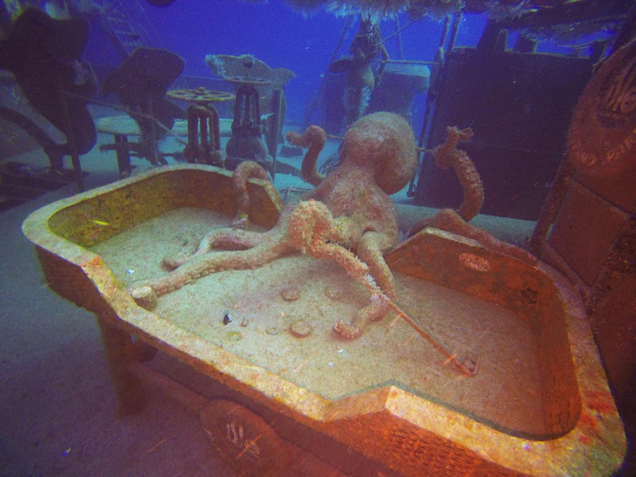 The statue of an octopus unfurls its tentacles across and around the edges of a craps table sitting on the deck of a shipwreck
