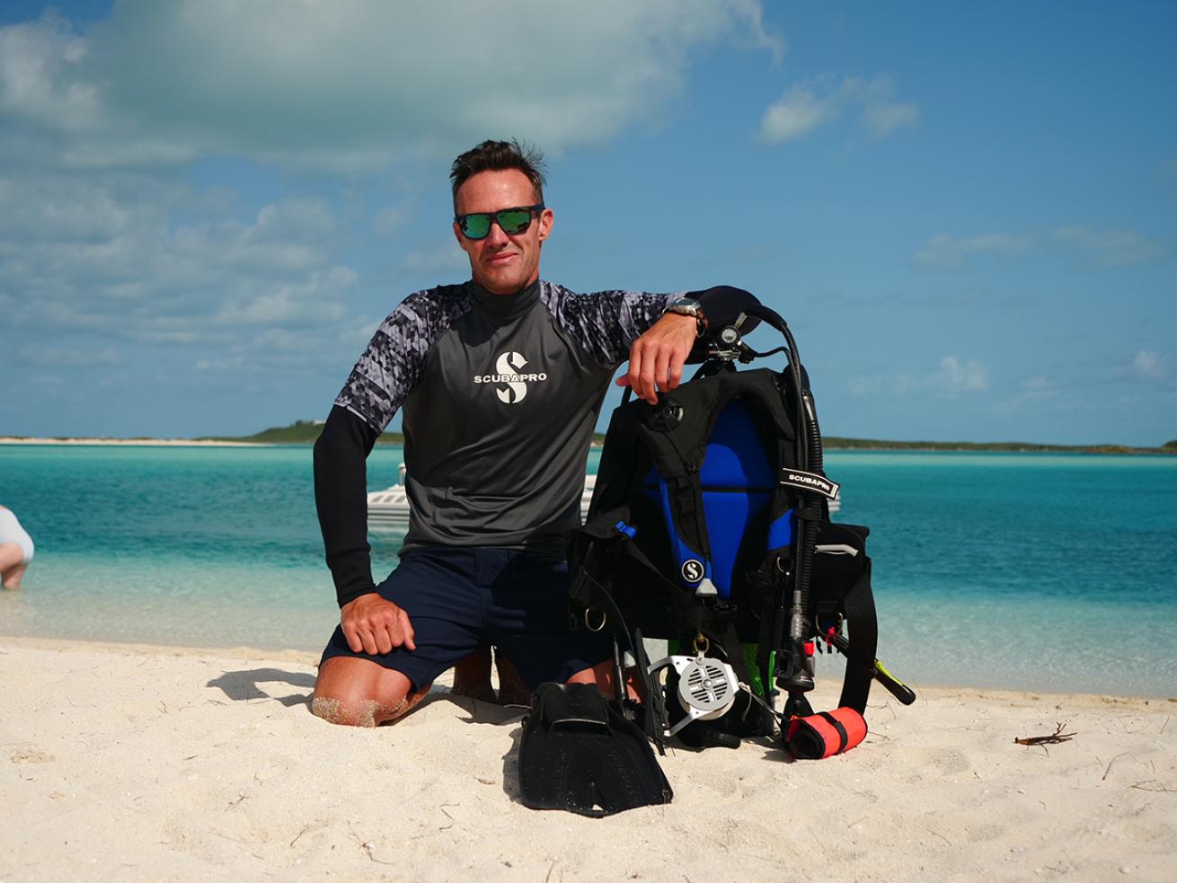 Male diver kneeling on beach by assembled scuba kit