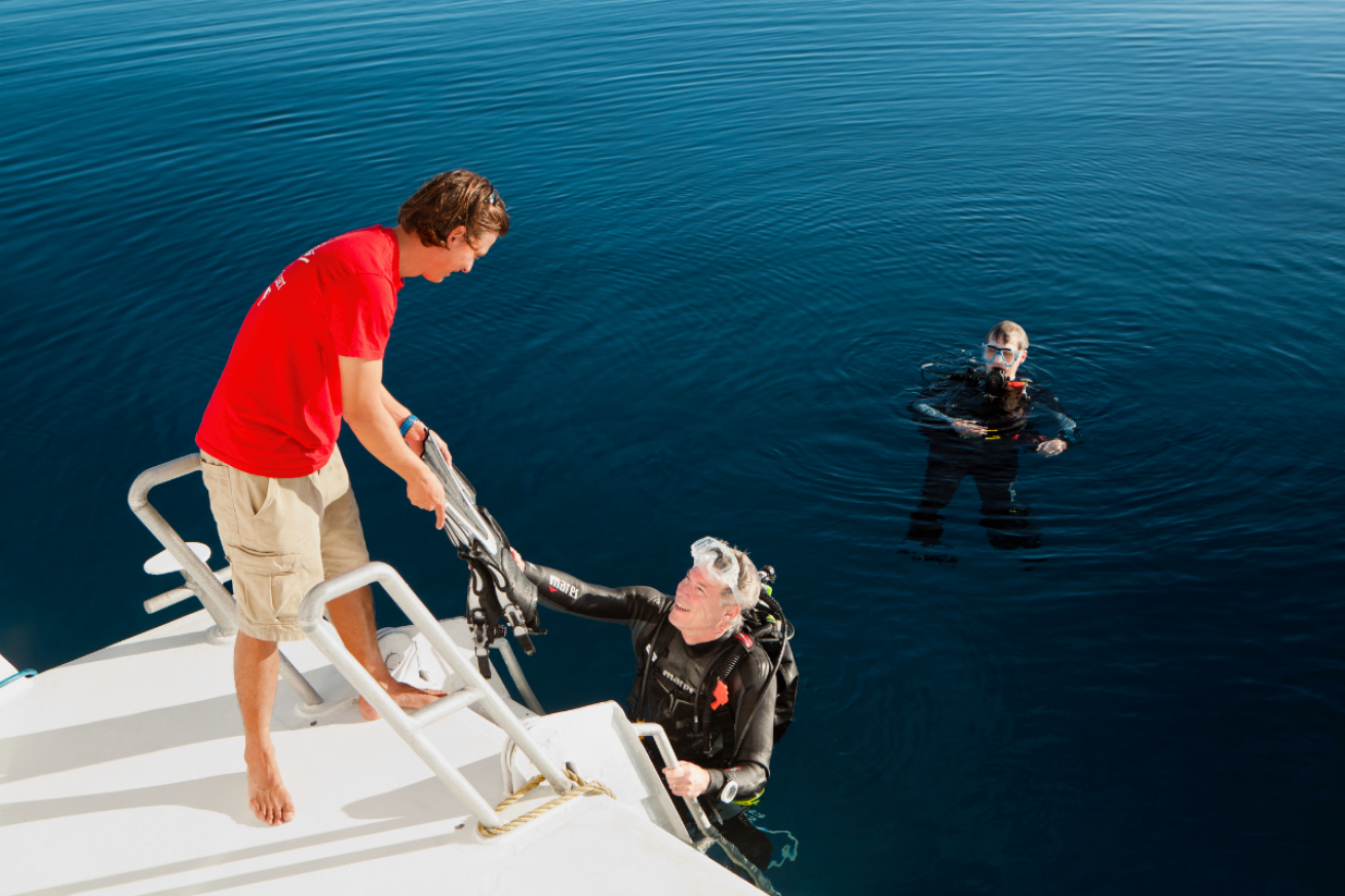 Two males in scuba diving gear climbing a ladder onto a boat
