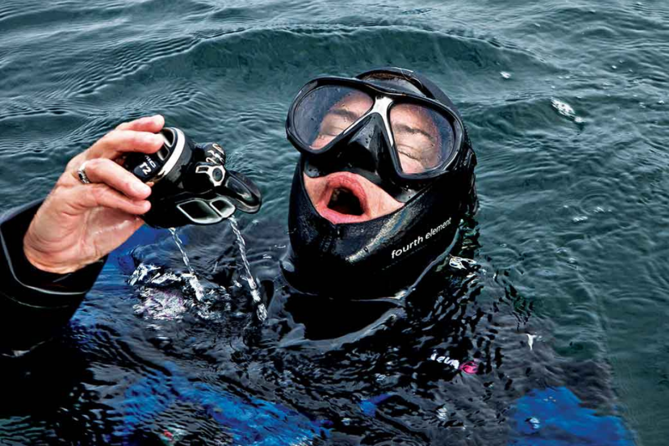 A person wearing a scuba diving mask and holding a regulator