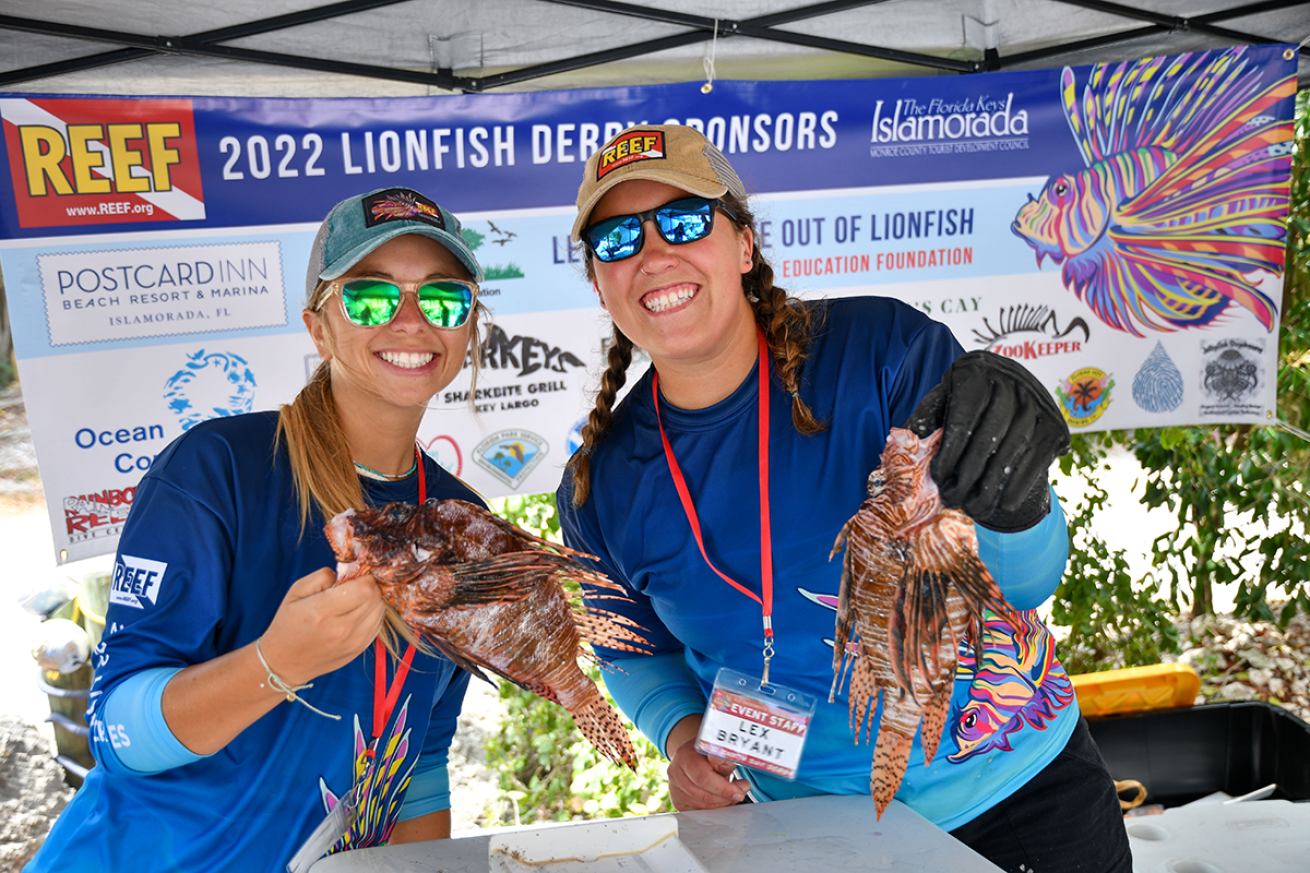 Two women in a tent hold lionfish
