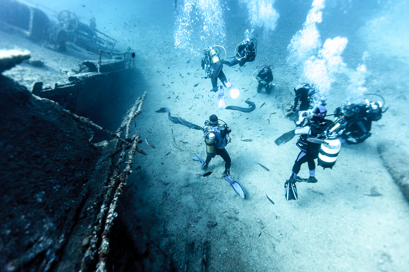 Divers crowd around a ship wreck.
