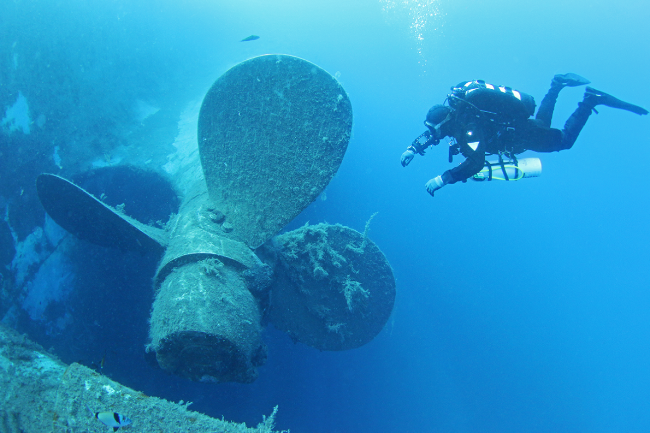 A diver swimming towards a ship propellor.