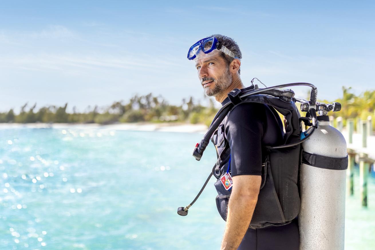 A male standing near water with scuba diving gear on