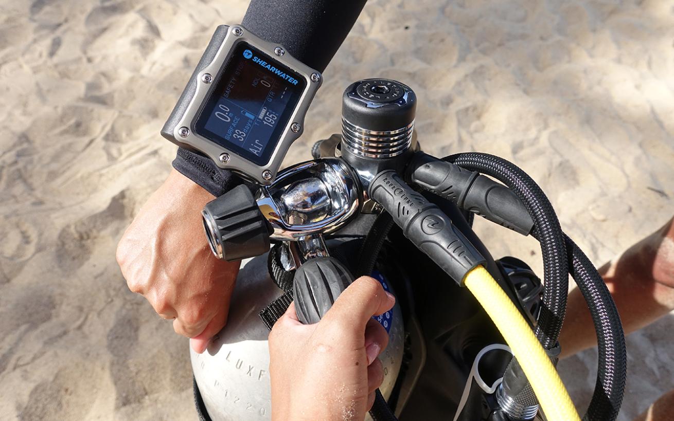 Person adjusting tank valve looking at dive computer on their wrist
