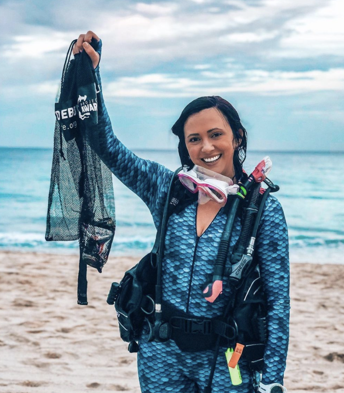 women holding a mesh bag in scuba gear on the beach cleaning trash