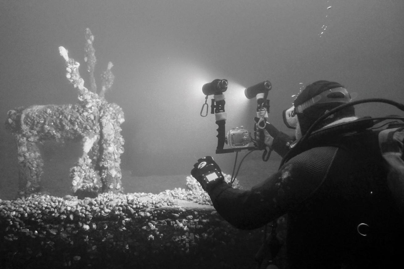 A diver takes a photo of the wooden ship’s wheel near the stern of the *O.J. Walker*. The well-preserved wreck is 86 feet long and rests at a depth of about 65 feet.