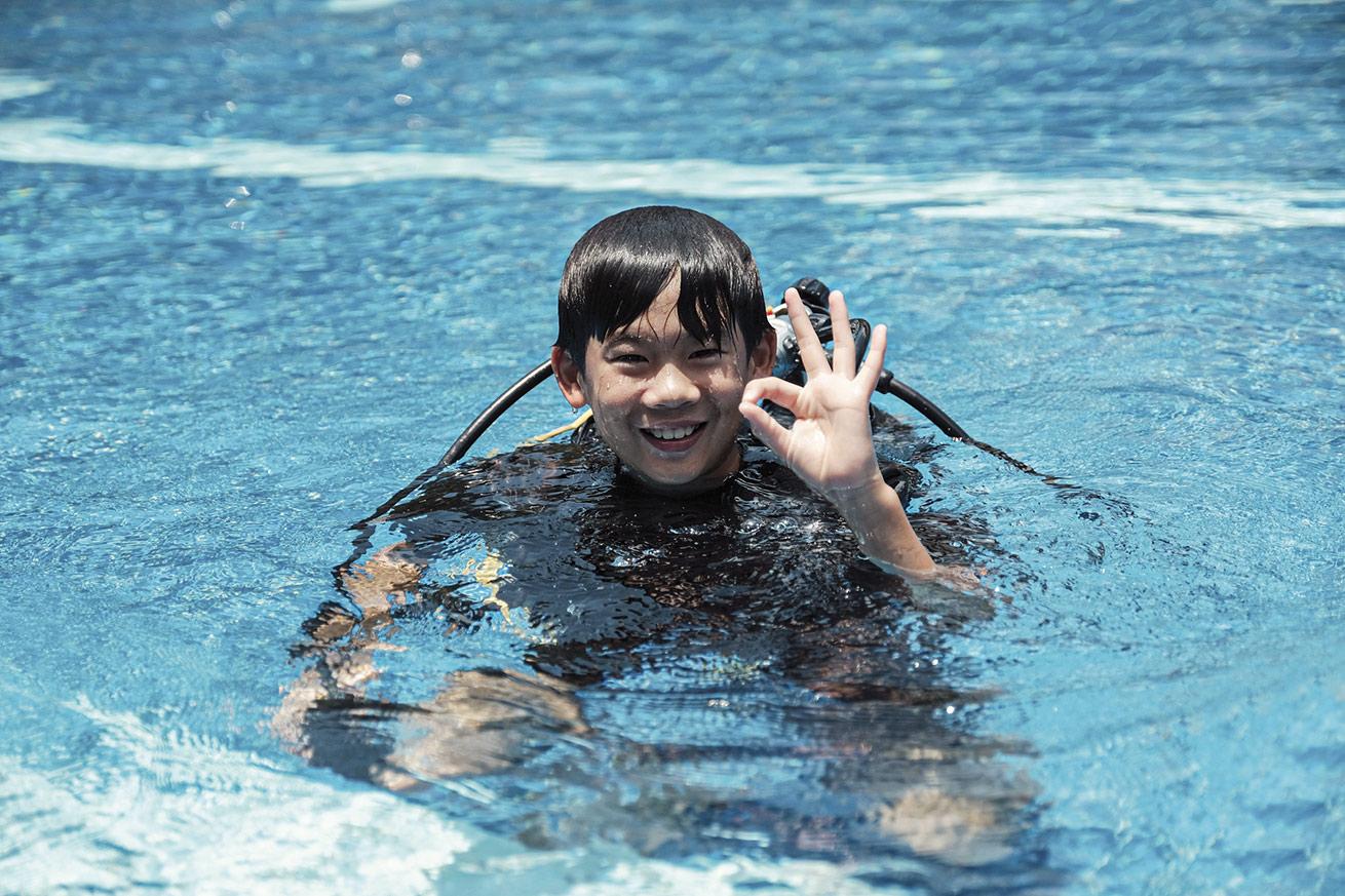 a child giving the okay symbol in a pool in scuba gear