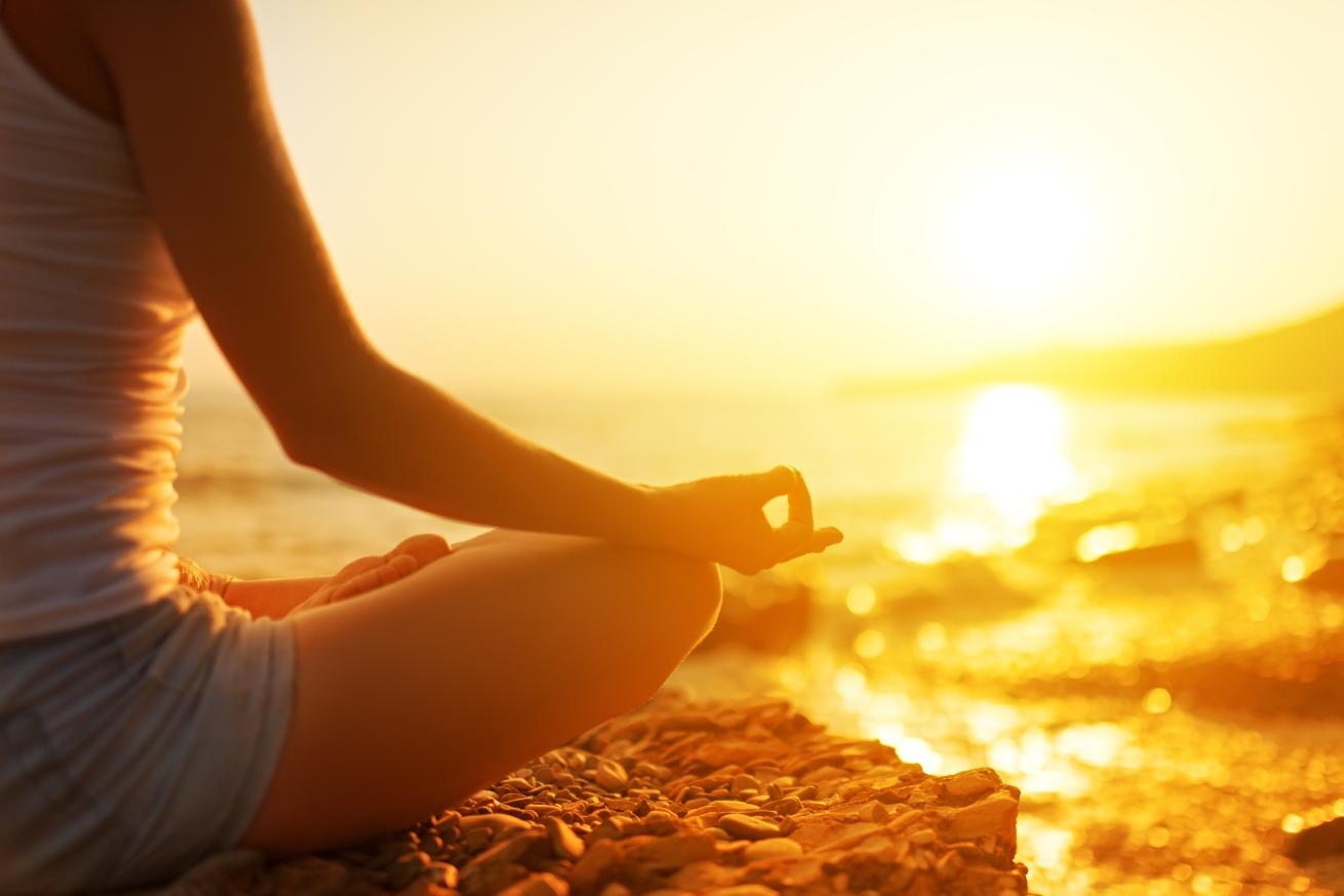a person sitting in a yoga pose by the ocean at golden hour