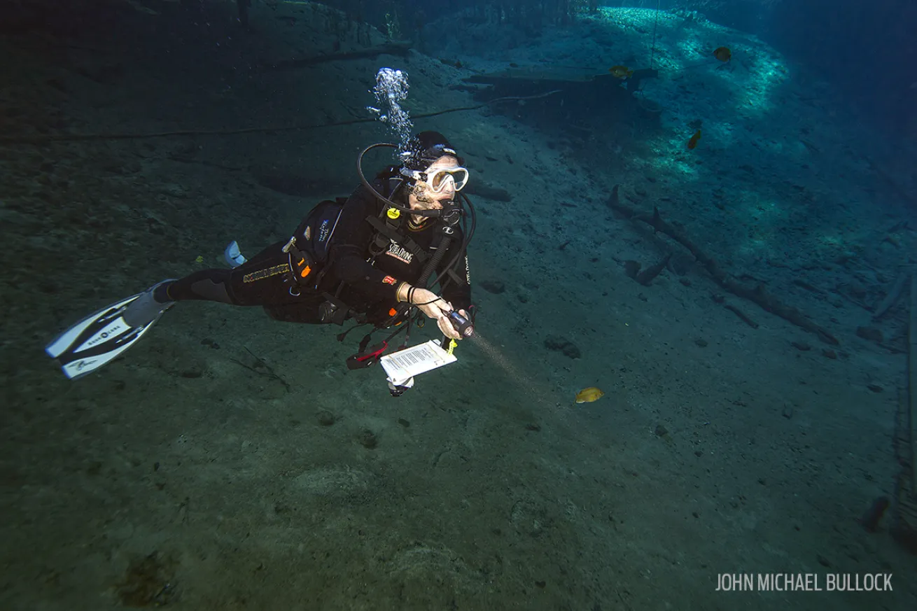 Scuba diver shines her light while exploring underwater cavern
