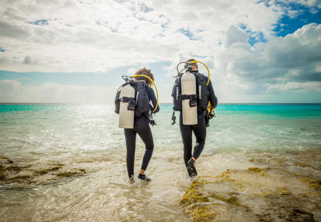 A couple of people wearing scuba gear walking in the water
