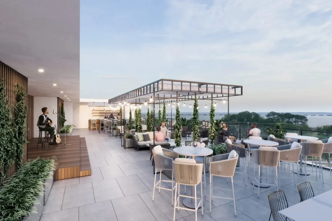 Photograph of a modern rooftop lounge in Pensacola, Florida, featuring seating areas with tables and chairs, a small stage with a musician, and a pergola adorned with hanging plants and string lights.