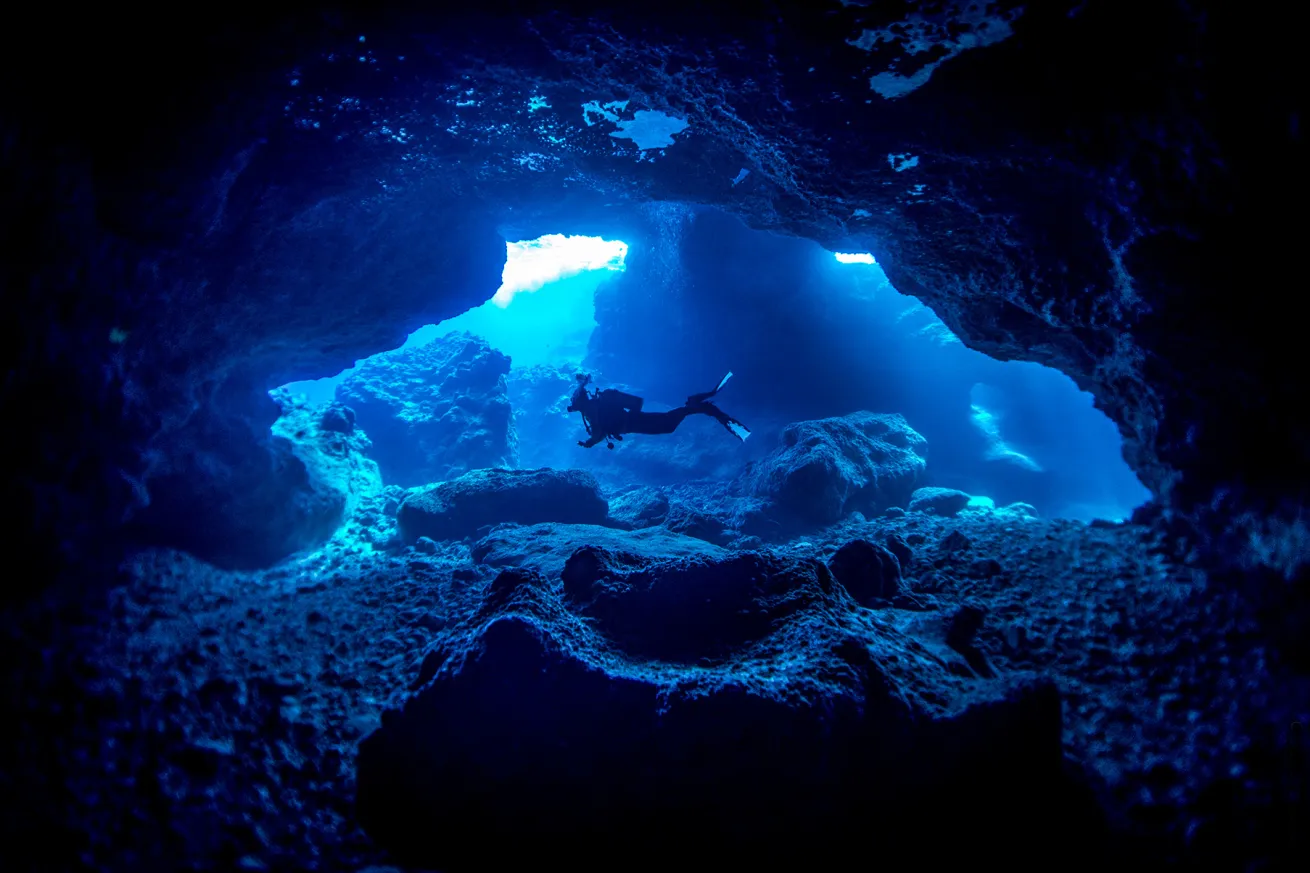 divers gliding through a cavern in niue