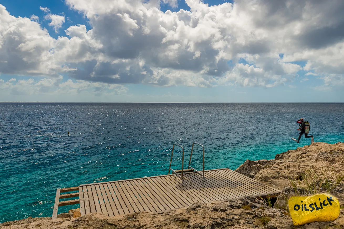Scuba diver in Bonaire doing a giant stride into crystal-clear warm water. 