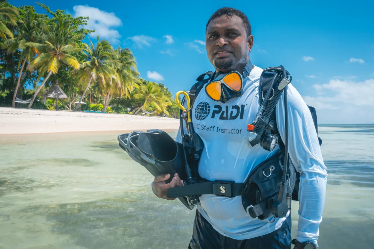 scuba diver holding gear in water on tropical beach