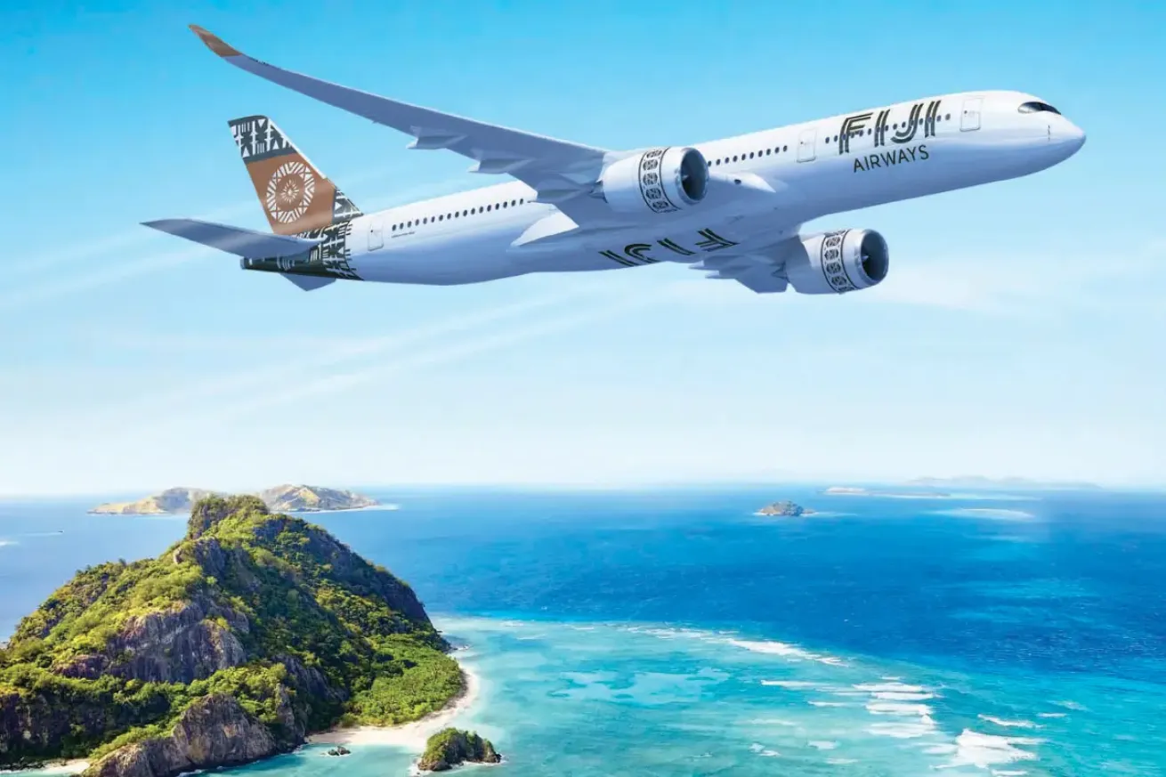 Fiji Airways airplane flying over tropical islands and turquoise ocean, representing travel to a Fiji dive vacation.