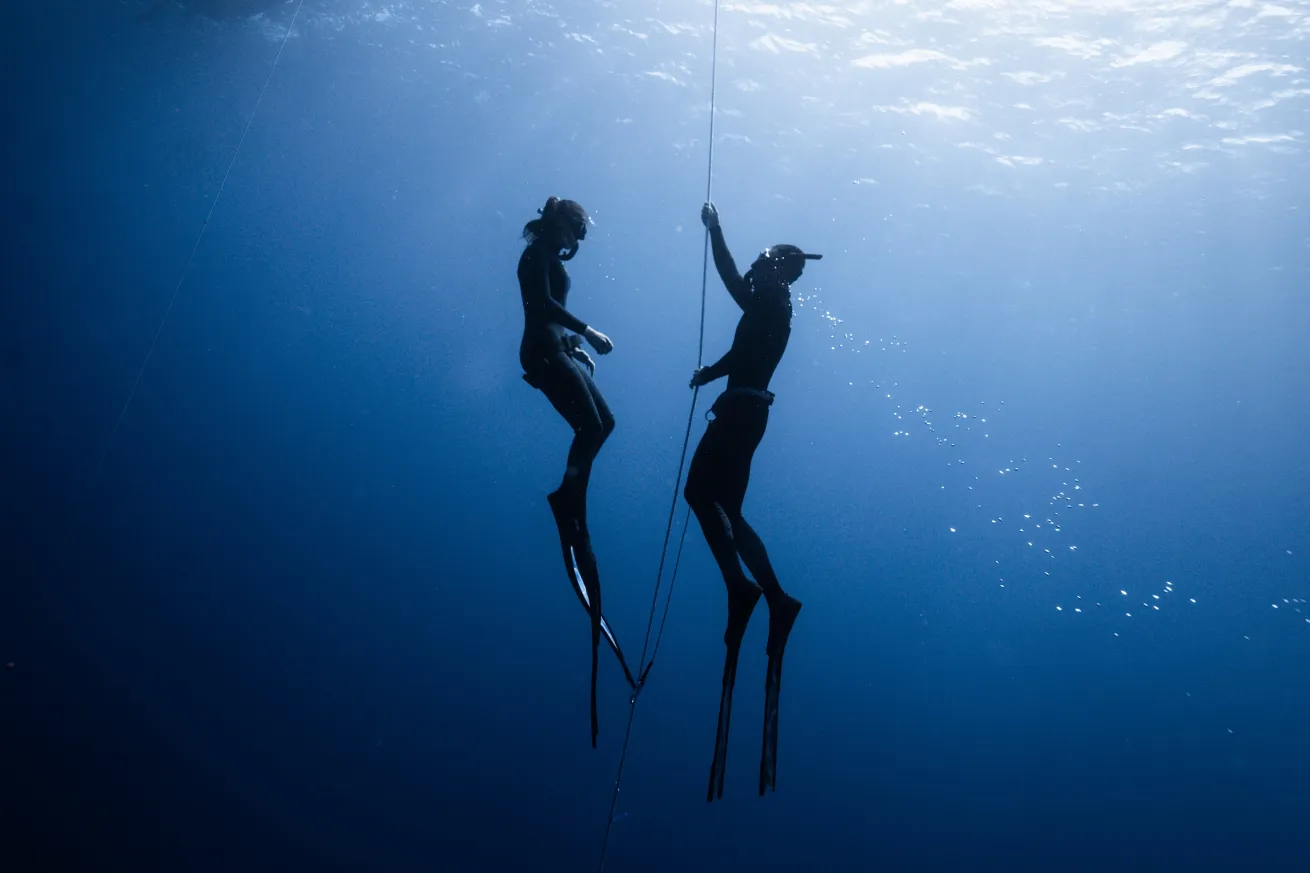 two divers during a freediving class, blue water surrounding two divers on a line