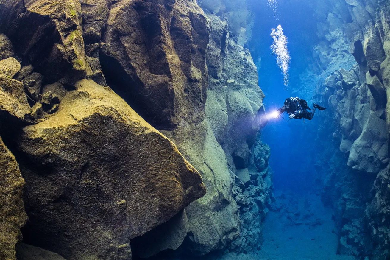 A diver swims through the Silfra Fissure, a crack in the Earth's crust between the North American and Eurasian continental plates that is filled with glacial melt water. In this photo, the American plate is on the right.