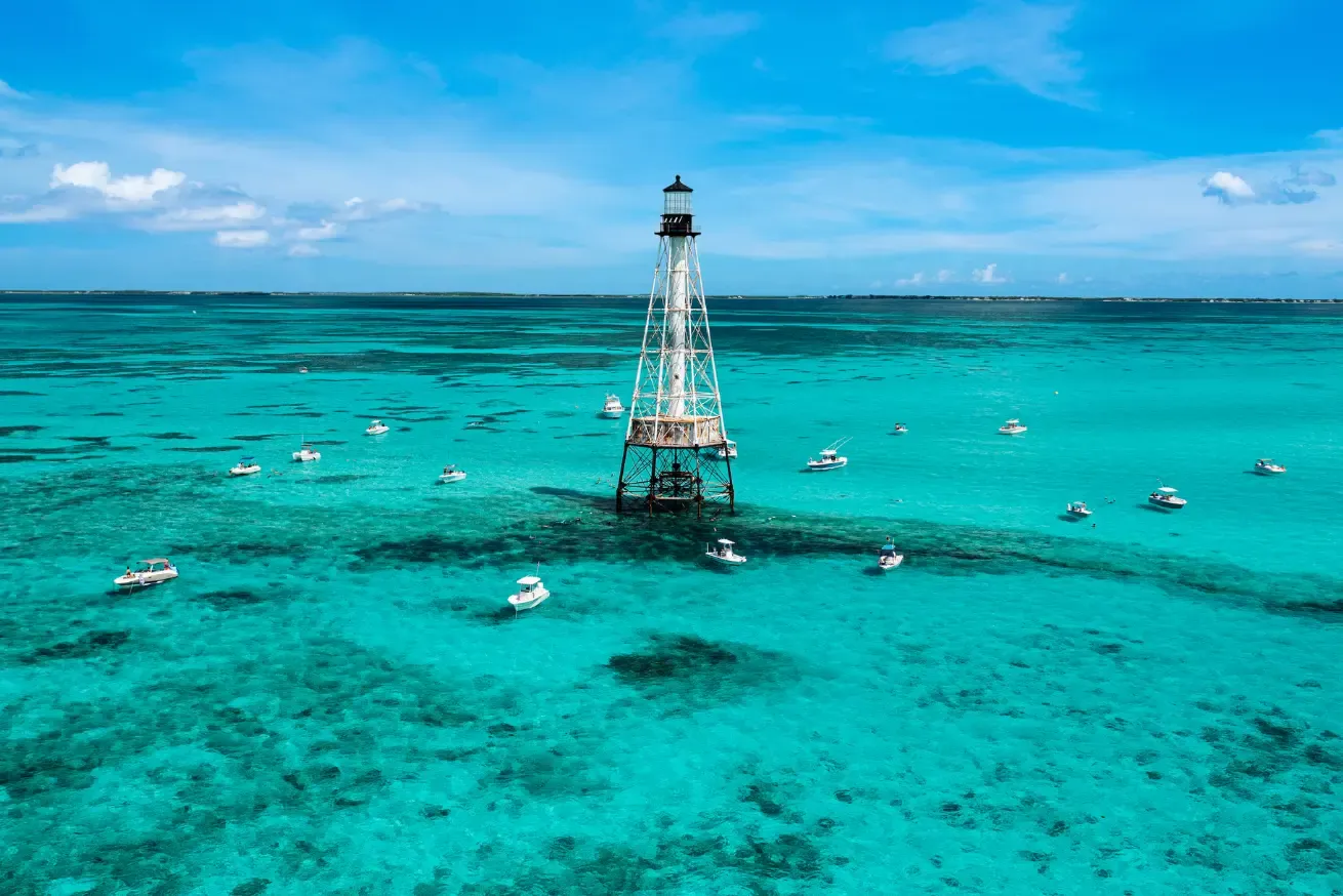 Photograph of Alligator Reef in Islamorada showing a tall, metal lighthouse standing in clear turquoise ocean waters surrounded by numerous small white boats.
