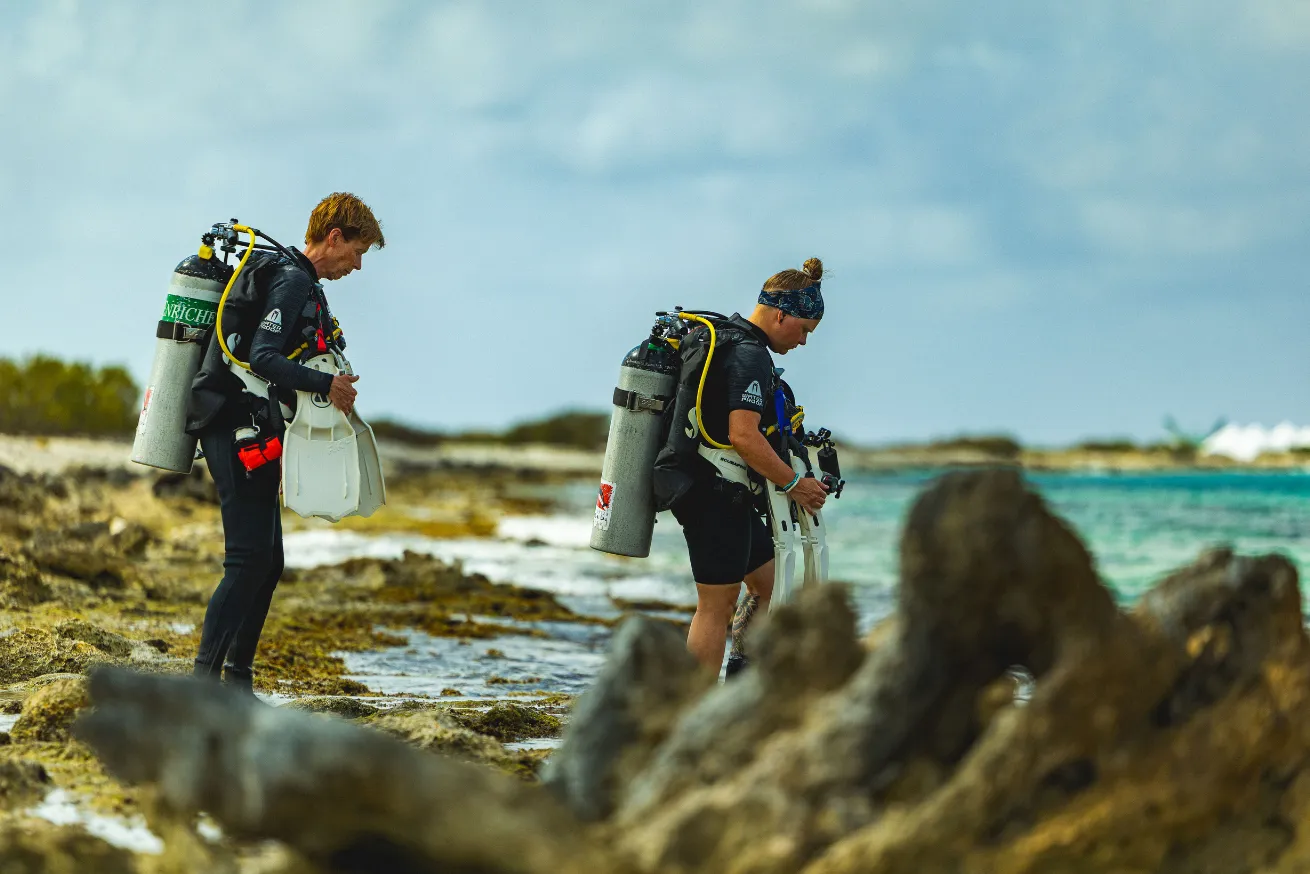 Two female scuba divers walking into the ocean in Bonaire. 