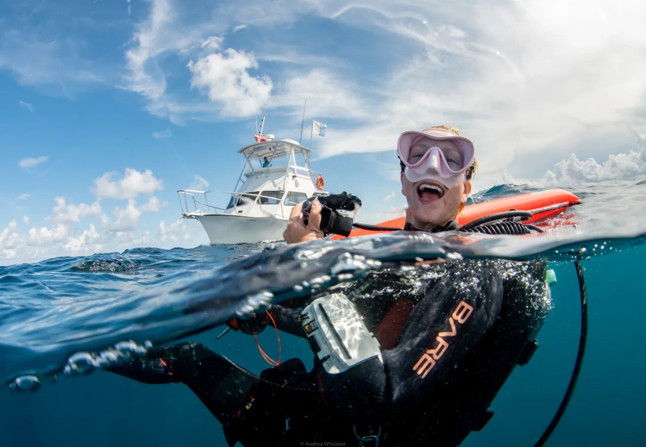 A person in a scuba gear in the water with a boat in the background