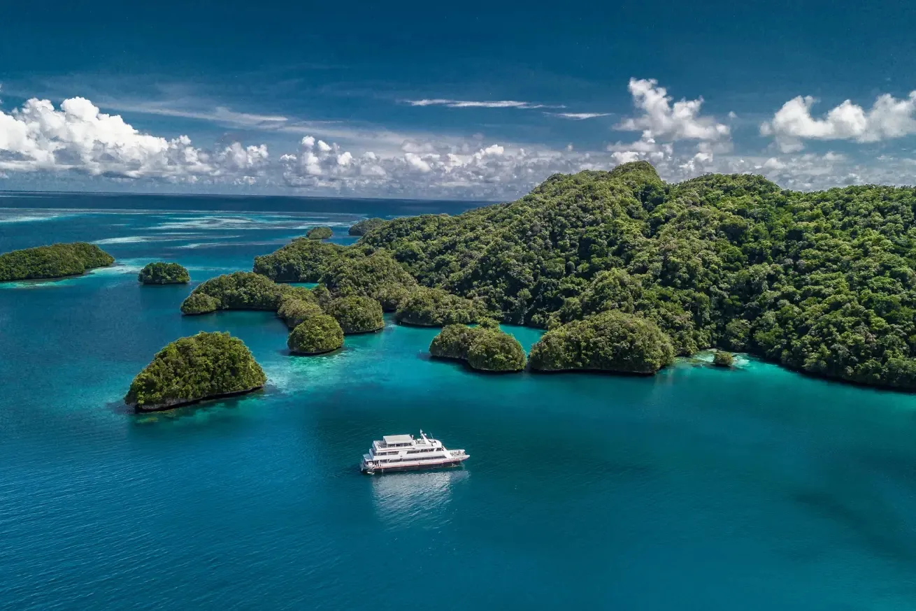 Aerial photograph of a tropical seascape featuring The Palau Aggressor II near multiple small, lush green islands surrounded by clear blue water.