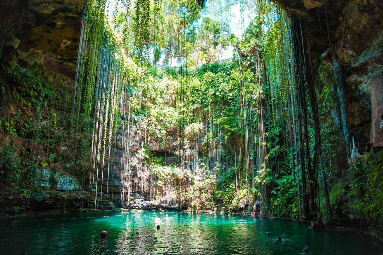 People swimming in a cenote pool with Ik Kil in the background