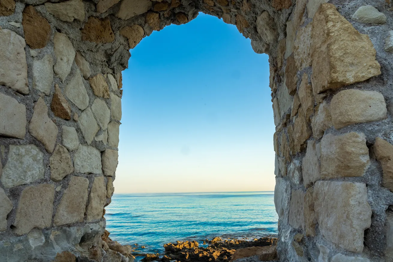 Outlook through arched opening or window to Mediterranean horizon and morning sky in bastion structure on lighthouse walkway at Chania, Crete.