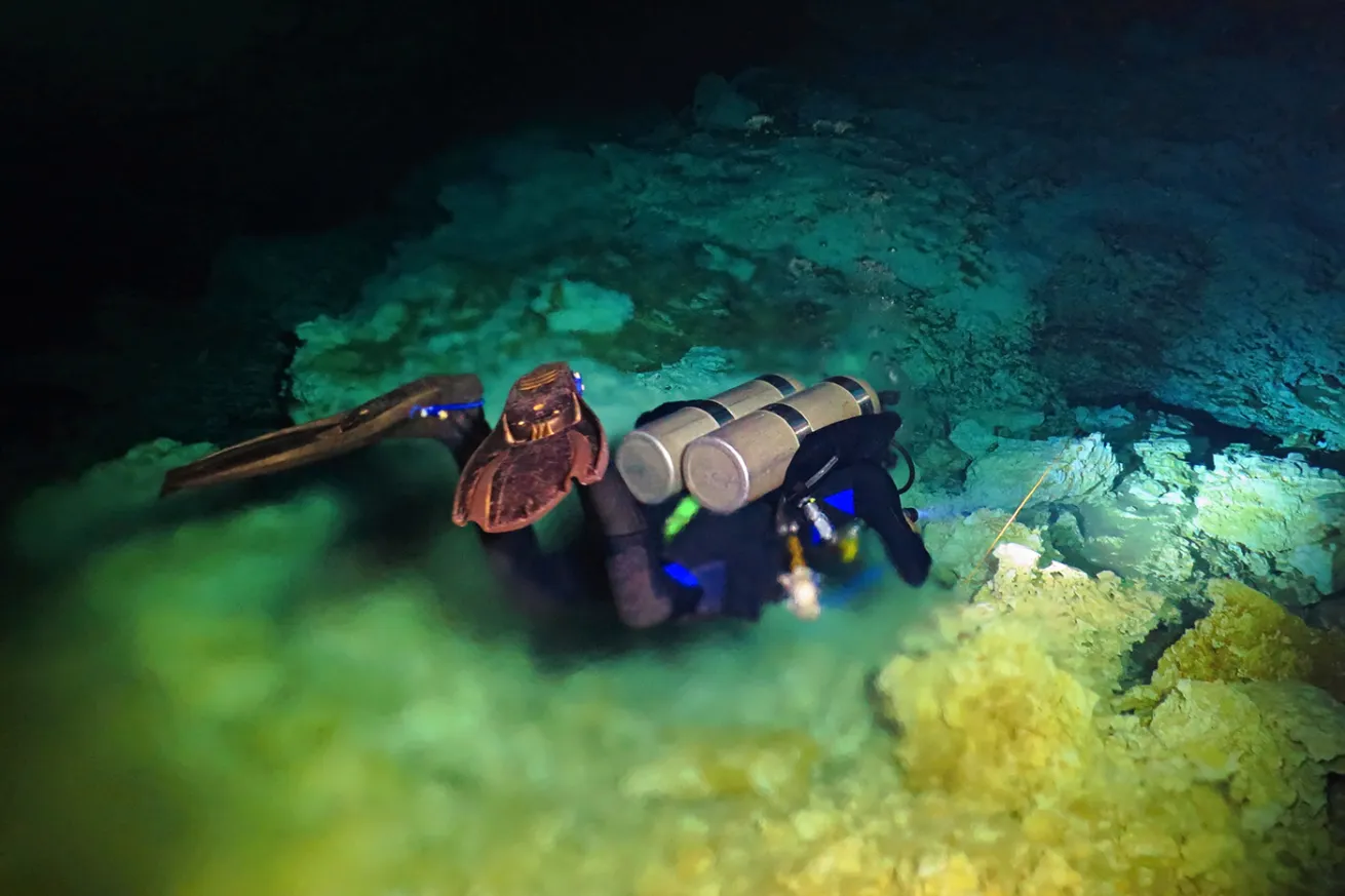 Cave diver descending from clear freshwater into distorted-looking saltwater signifying halocline