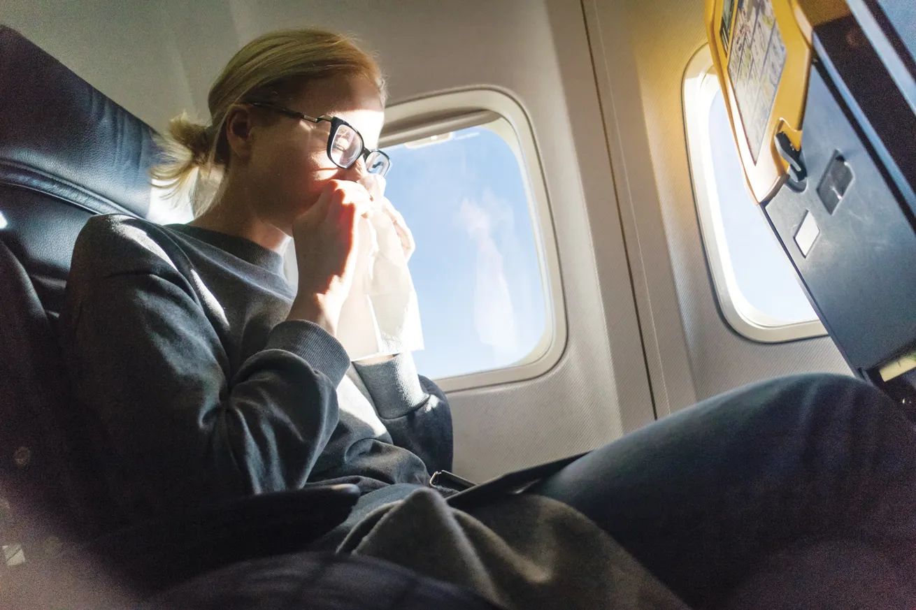 a woman on a plane with a tissue held up to her nose